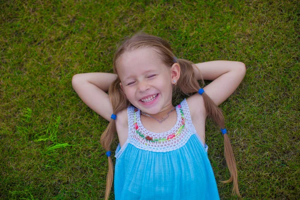 Little girl lying on the grass near the house and laughs — Stock Photo, Image