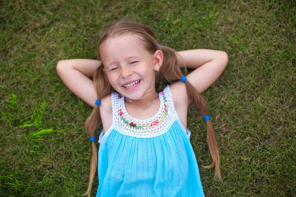 Little girl lying on the grass near the house and laughs — Stock Photo, Image