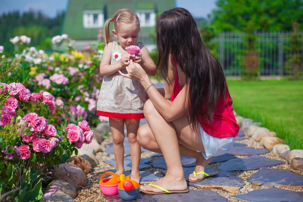 Joven madre con su hermosa hija oliendo flores en el jardín —  Fotos de Stock