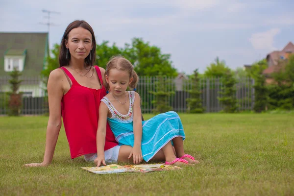 Young mother and her cute daughter reading book and enjoying holiday — Stock Photo, Image