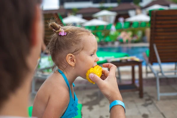Young father feeds his little daughter corn near the swimming pool — Stock Photo, Image