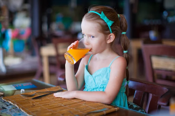 Adorable little girl having breakfast and drinking juice at resort restaurant — Stock Photo, Image