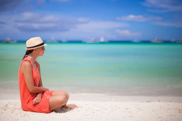 Rear view of young sexy woman in hat sitting on white sand beach — Stock Photo, Image