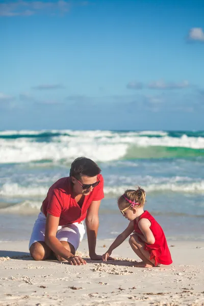 Молодий батько і його чарівна маленька дочка малюють на піску на пляжі — стокове фото