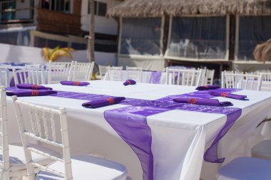 kumlu sahilde mor yay ile süslenmiş beyaz düğün masa