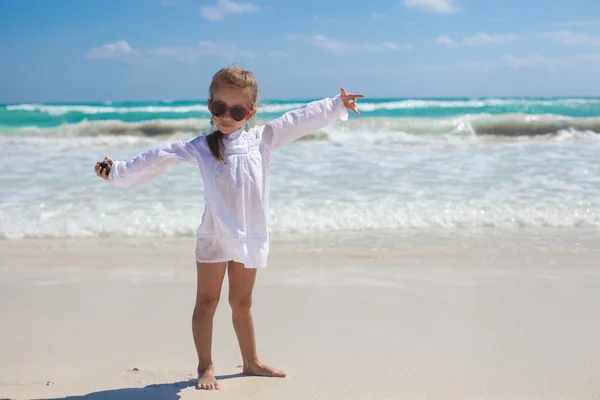 Красивая маленькая девочка раскинула руки, стоя на белом пляже — стоковое фото