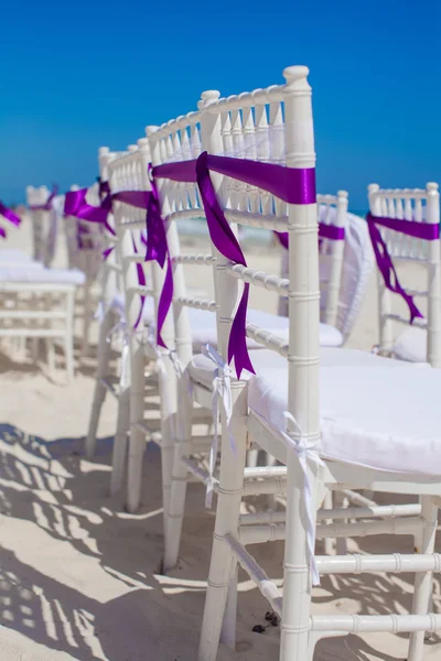 Cadeiras de casamento branco decorado com arcos roxos na praia de areia — Fotografia de Stock