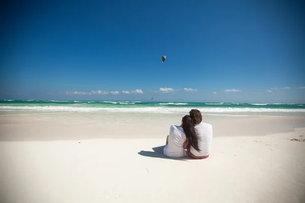 Bakifrån av unga paret sitter vid tropiska vita stranden — Stockfoto