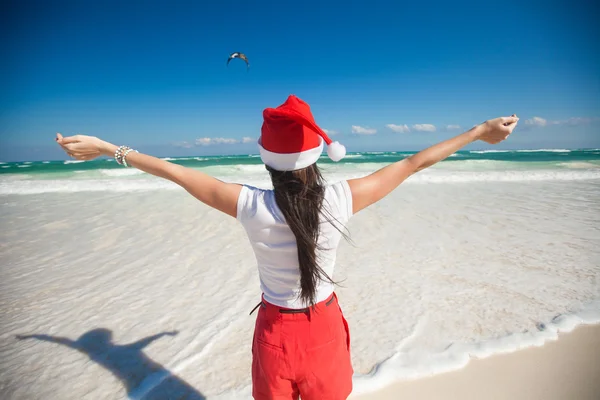 Vista posteriore di bella ragazza in cappello di Babbo Natale a piedi come un uccello sulla spiaggia bianca — Foto Stock