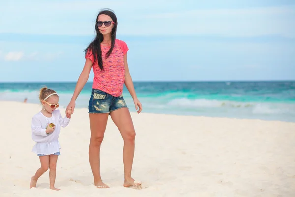 Jonge mooie moeder en haar schattige kleine dochter lopen op wit zonnige strand — Stockfoto