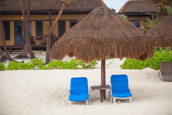 Kék nyugágyakat esős strandon nádfedeles napernyők alatt — Stock Fotó