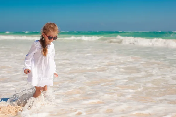 Cute toddler girl in white dress standing in shallow water at exotic beach — Stock Photo, Image