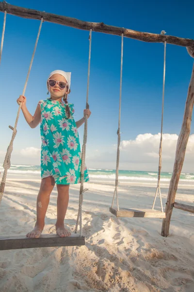 Adorable cute little girl in a dress and sunglasses on swing on white sandy Caribbean beach — Stock Photo, Image