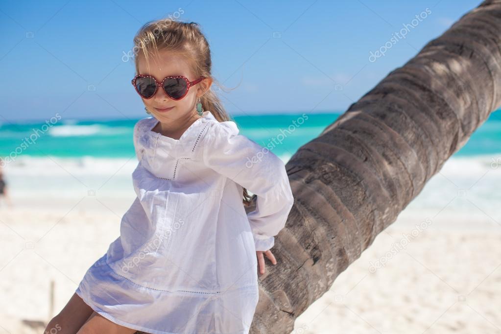 Closeup of little cute girl sitting on palm tree at the perfect caribbean beach