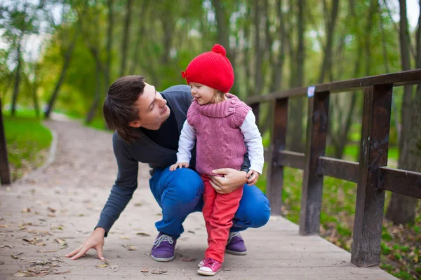 Porträt eines jungen Vaters, der mit seiner süßen Tochter im Herbstpark spazieren geht — Stockfoto
