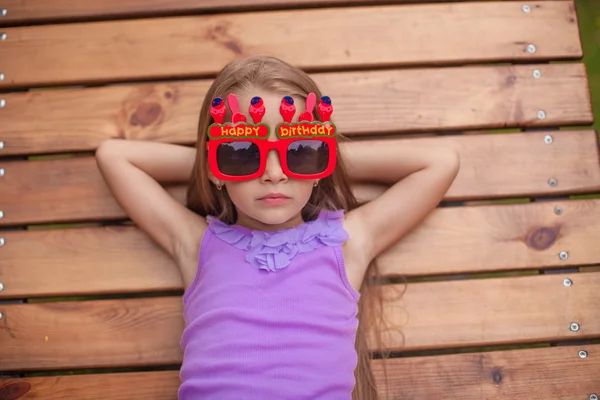 Очаровательная маленькая девочка в очках со словами "С днем рождения на открытом воздухе" — стоковое фото