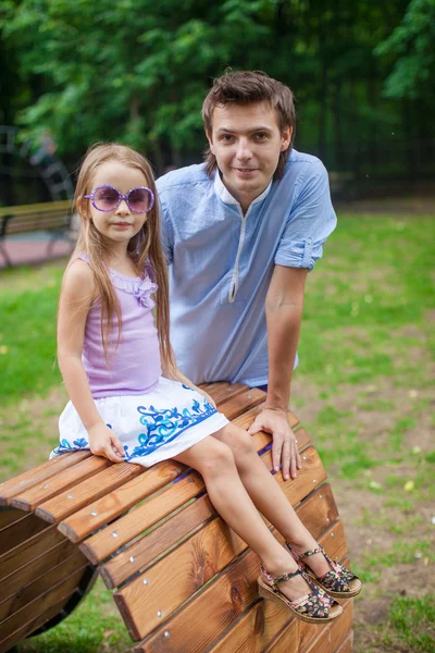 Портрет отца с дочерью, сидящей на деревянной доске кровати в парке — стоковое фото
