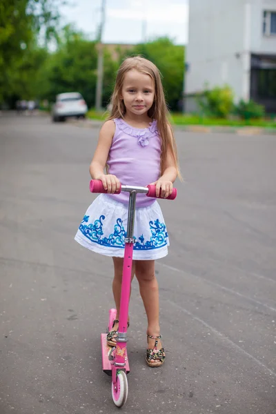 Fashion adorable little girl on a scooter in the street — Stock Photo, Image