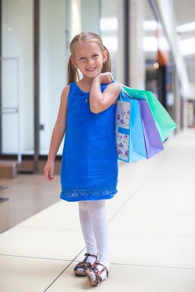 Pequena menina feliz com pacotes em um grande centro comercial — Fotografia de Stock