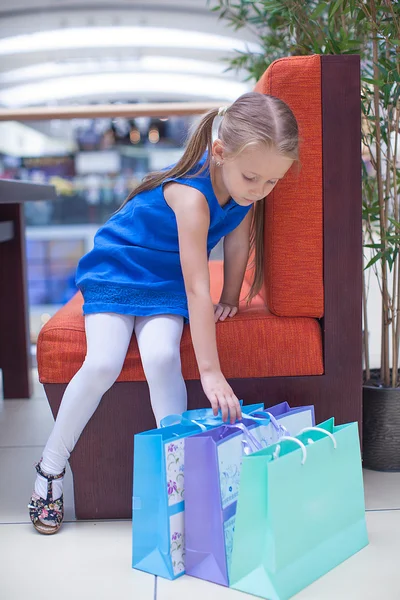 Küçük kız moda paketler halinde büyük bir alışveriş merkezi yakınında oturuyor. — Stok fotoğraf