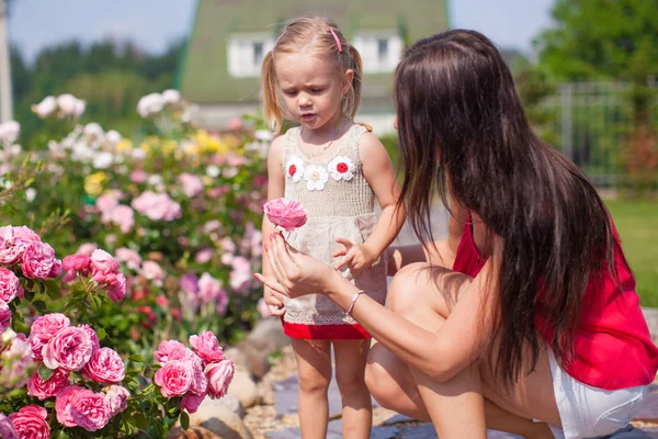 Joven madre con su hermosa hija oliendo flores en el jardín — Foto de Stock