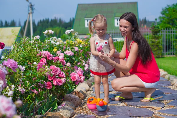 Young mother with her cute daughter near flowers in the garden — Stock Photo, Image