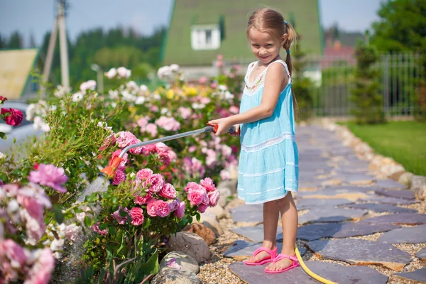 Menina bonito em flores de rega vestido azul com uma mangueira em seu jardim — Fotografia de Stock