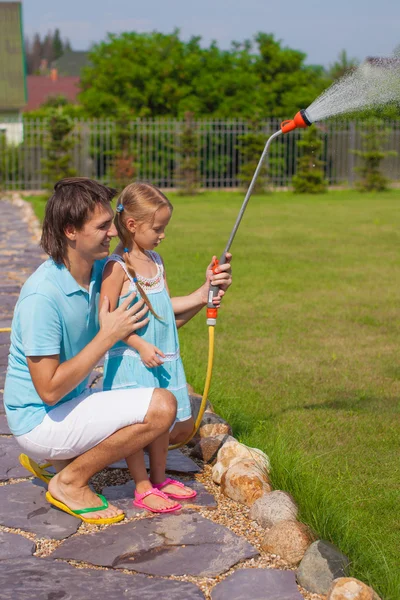 Little cute girl and father watering flowers with hose in their garden — Stock Photo, Image