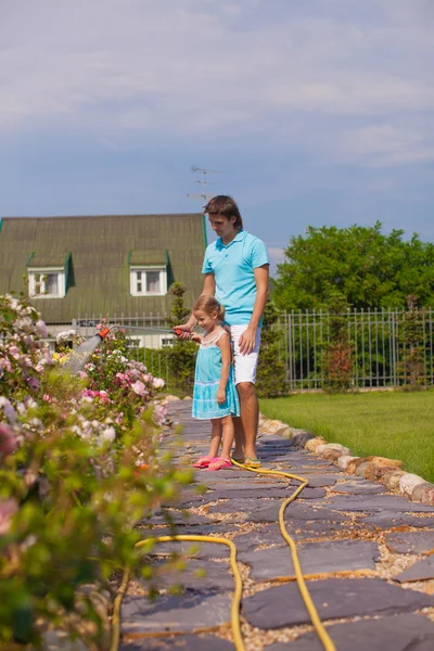 Piccola ragazza carina e padre irrigazione fiori con tubo nel loro giardino — Foto Stock