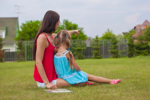 Young mother and her cute daughter enjoying the holiday on grass near house — Stock Photo, Image