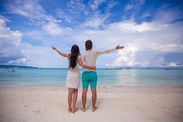 Back view of young couple spread their arms standing on white sandy beach — Stock Photo, Image
