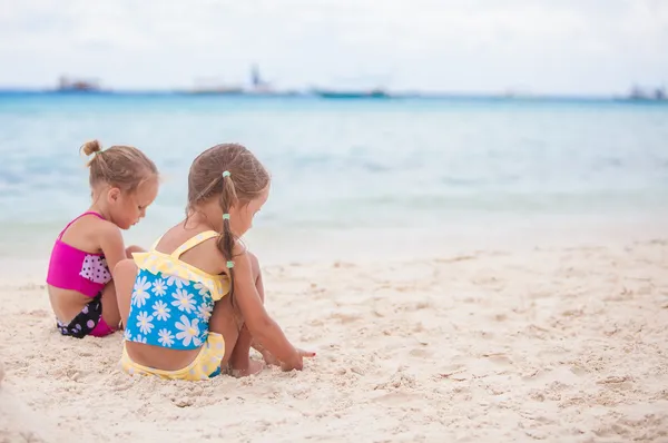 Två små systrar i fina baddräkter spelar på sandstranden — Stockfoto