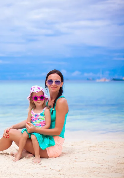 Young beautiful mother and her little daughter sitting on white beach — Stock Photo, Image