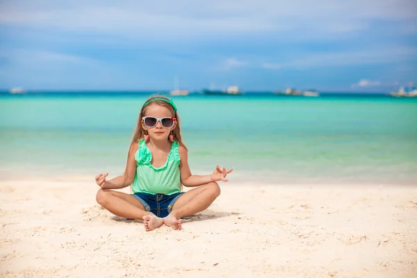 Beautiful little girl sitting in a lotus position on an exotic beach — Stock Photo, Image