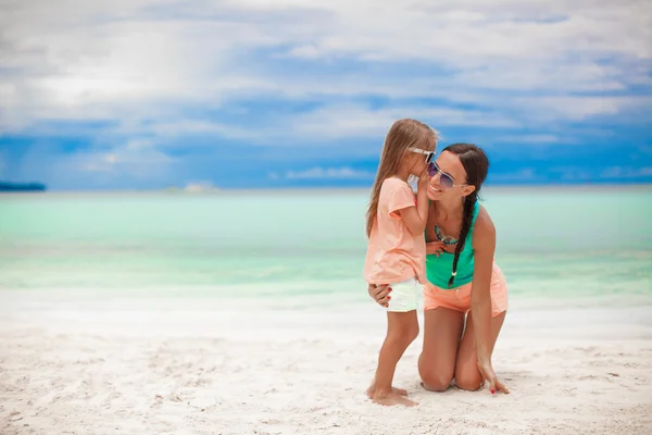 Joven madre y su linda niña susurrando en la playa blanca — Foto de Stock