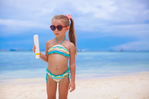 Kleines entzückendes Mädchen im Badeanzug hält eine Flasche Sonnencreme in der Hand — Stockfoto