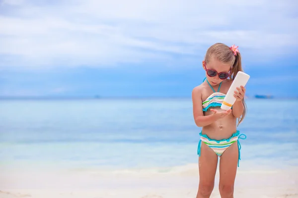 Kleines entzückendes Mädchen im Badeanzug hält eine Flasche Sonnencreme in der Hand — Stockfoto