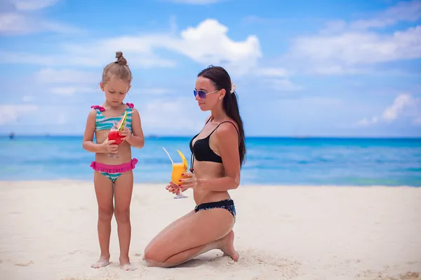 Happy mother and her adorable little daughter with juice at tropical beach — Stock Photo, Image