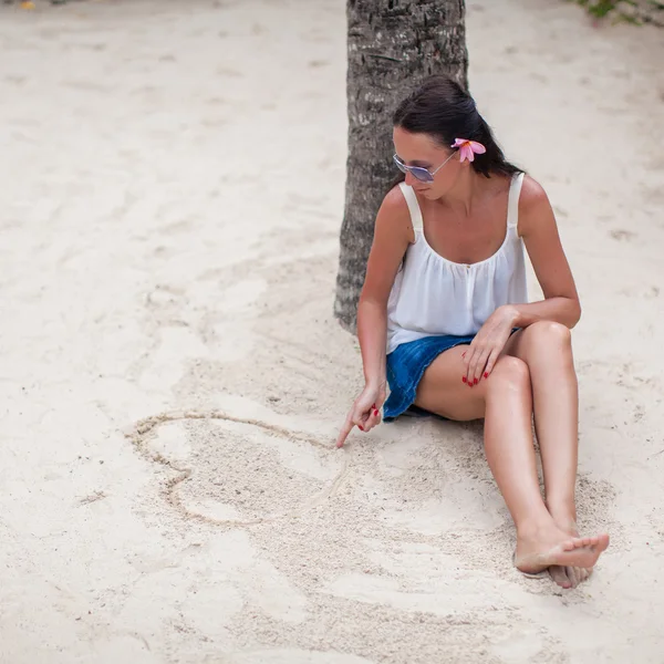 Young woman draws a heart in the sand with her finger — Stock Photo, Image