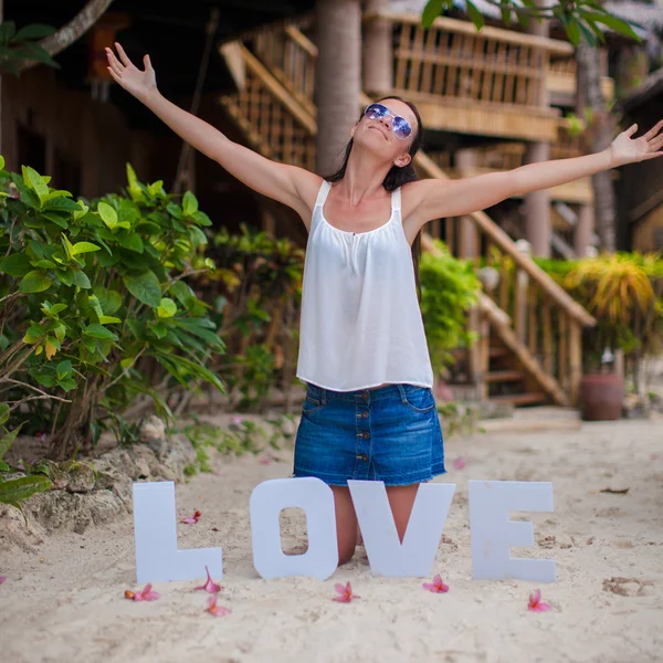 Jong meisje, zittend op zand met het woord "liefde" en verspreiden van haar armen — Stockfoto