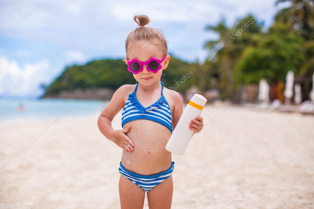 Little adorable girl in swimsuit rubs sunscreen herself