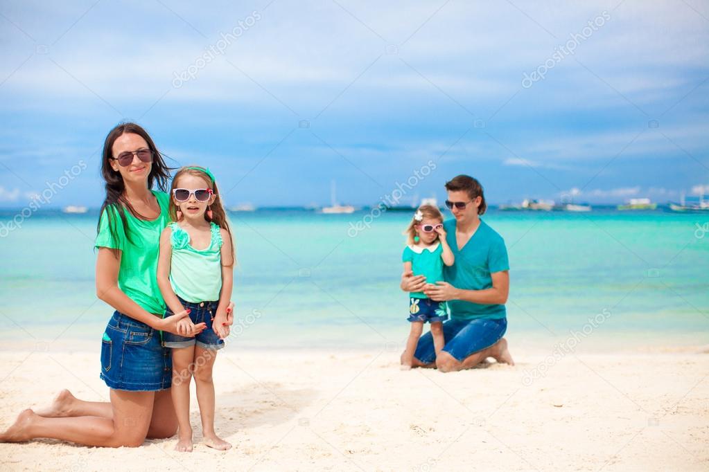 Mom with her older daughter in the foreground and dad with youngest daughter in the background on the beach