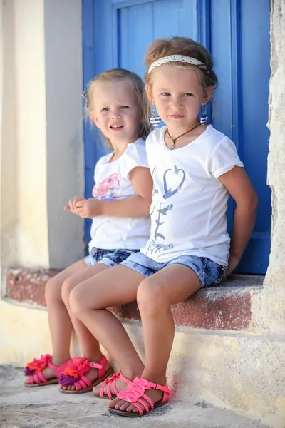 Duas meninas adoráveis sentadas na porta da casa velha na aldeia Emporio, Santorini, Grécia — Fotografia de Stock