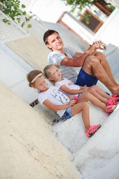 Happy father and cute daughters sitting on street in old greek town — Stock Photo, Image