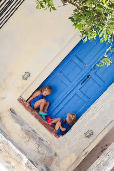 Lilla söta systrar sitter nära gammal blå dörr i grekiska byn emporio, santorini — Stockfoto