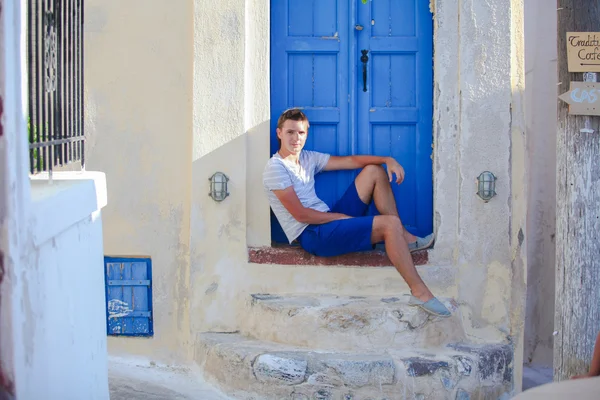 Ung man sitter nära gammal blå dörr av emporio byn på ön santorini, Grekland — Stockfoto