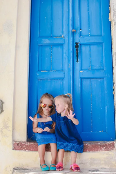 Αξιολάτρευτο κοριτσάκια που κάθονται κοντά παλαιά μπλε πόρτα στο ελληνικό χωριό του Εμπορειού, Σαντορίνη — Φωτογραφία Αρχείου