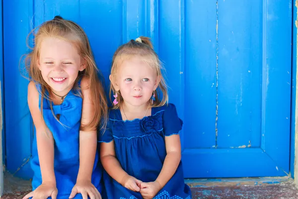 Closeup of Little adorable girls sitting near old blue door in Greek village, Emporio, Santorini — Stock Photo, Image