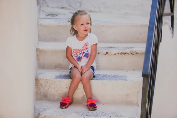 Linda niña sentada en los escalones de la antigua casa en Emporio pueblo, Santorini, Grecia —  Fotos de Stock