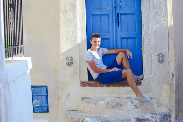 Młody człowiek siedzi w pobliżu starych drzwi niebieski emporio wioski na wyspie santorini, Grecja — Zdjęcie stockowe